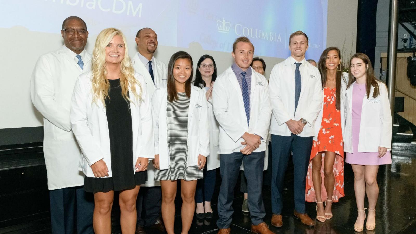 Group of students wearing white coats on stage