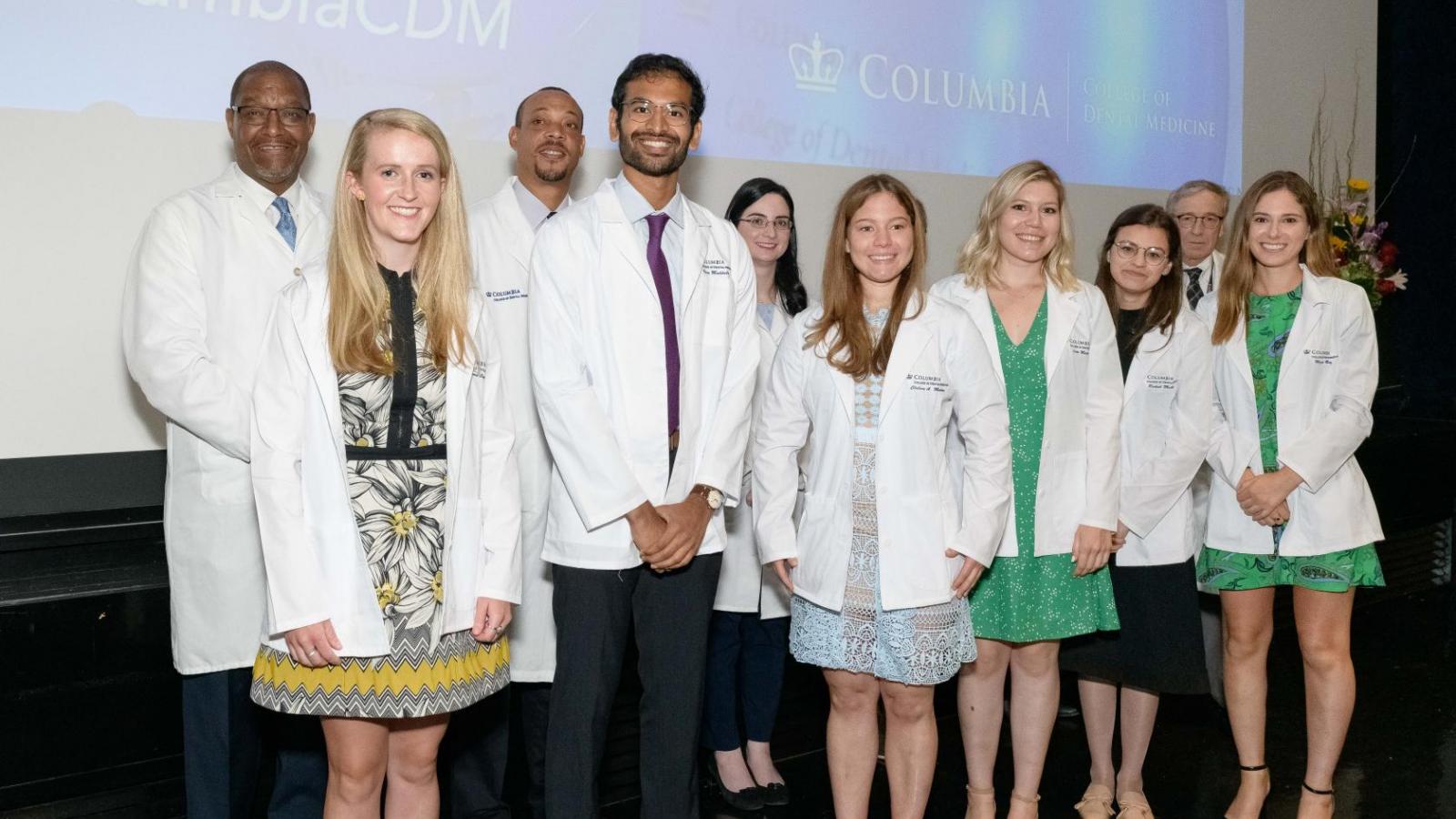Group of students wearing white coats on stage