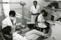 Image of one patient, one dentist and two students of the clinic. The male dentist is about to examine the patient. And other male and female students are observing him.