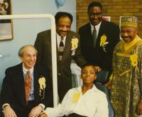 Picture from a school clinic opening in 2014. Four men are standing up and one female student is on the patient chair. They are are smiling at the camera