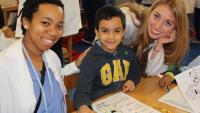 two dental students coloring with young child at a school