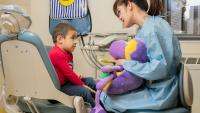 dentist holding stuffed animal and big toothbrush during kids exam
