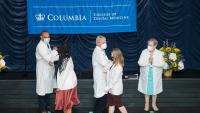 Two students giving elbow bumps to faculty members after donning their white coats