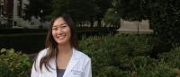 Student stands in white coat smiling