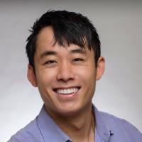 An adult male of Asian descent with a light and dark gray gradient in the background