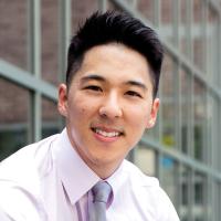 An adult male of Asian descent with a view of glass windows on a building in the background